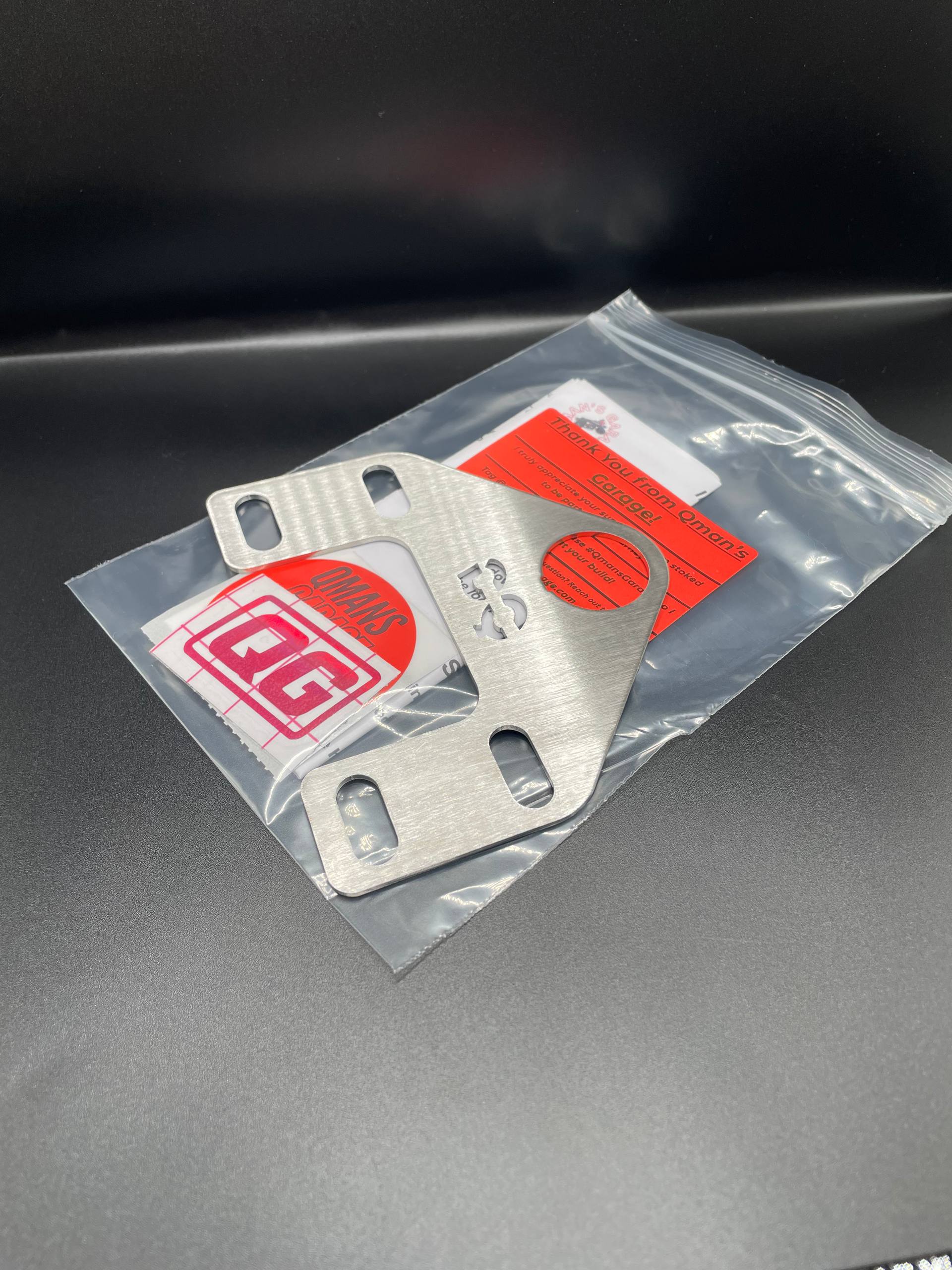 Metal bracket in clear packaging with a red label on a dark surface